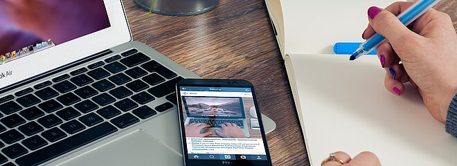 Mulher segurando um livrinho de notas, ao lado de um notebook e um celular
