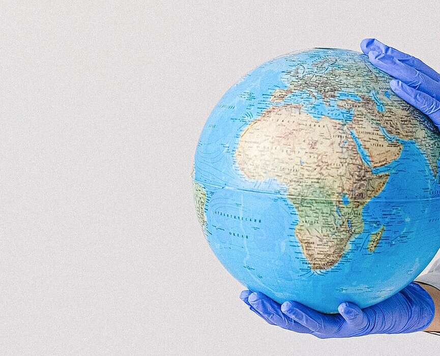 mulher de luvas e máscara segurando um globo do planeta