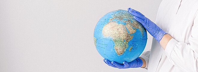 mulher de luvas e máscara segurando um globo do planeta