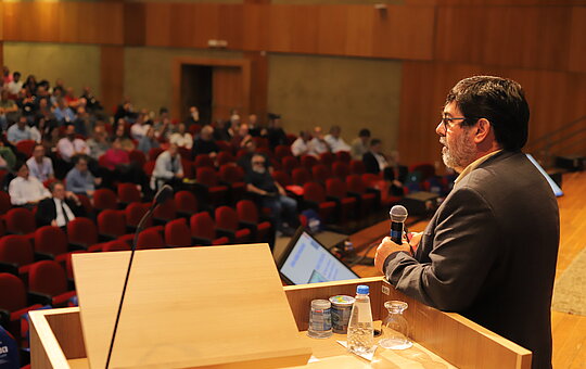 Na imagem, um auditório do Mackenzie com diversas pessoas ao fundo.
