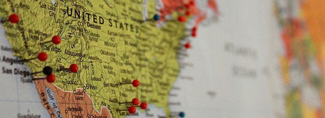 A imagem mostra um mapa, com os Estados Unidos em evidência e alguns alfinetes grudados em determinados locais. 