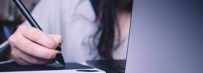 A foto mostra uma mulher escrevendo e um notebook na sua frente. Não conseguimos ver seu rosto. 