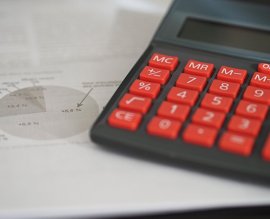 papel com gráficos sobre uma mesa ao lado de uma calculadora de teclas vermelhas.