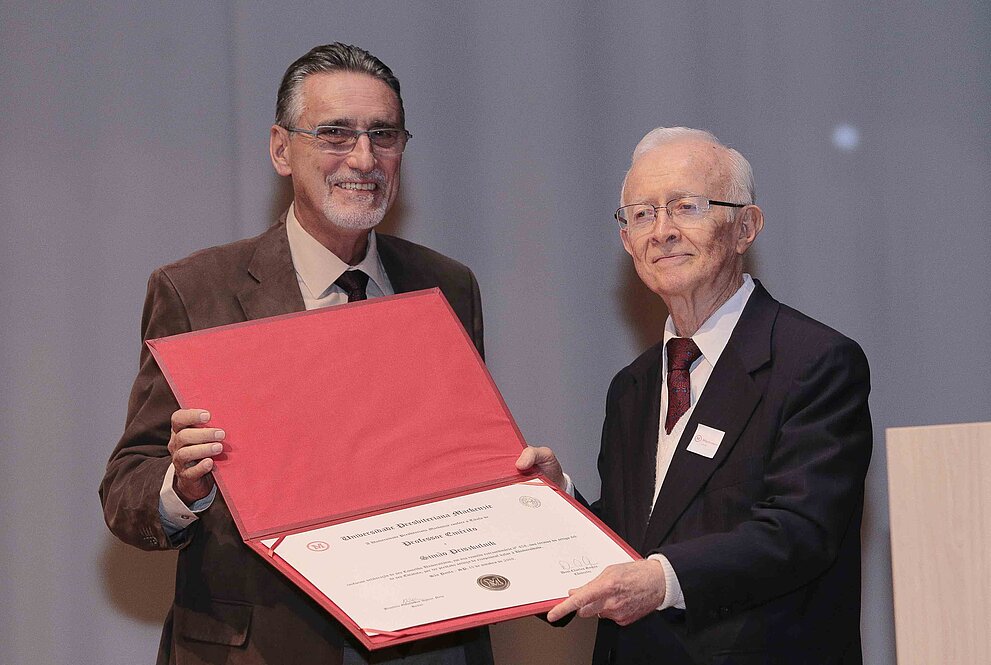 Um homem entrega um diploma para outro homem idoso