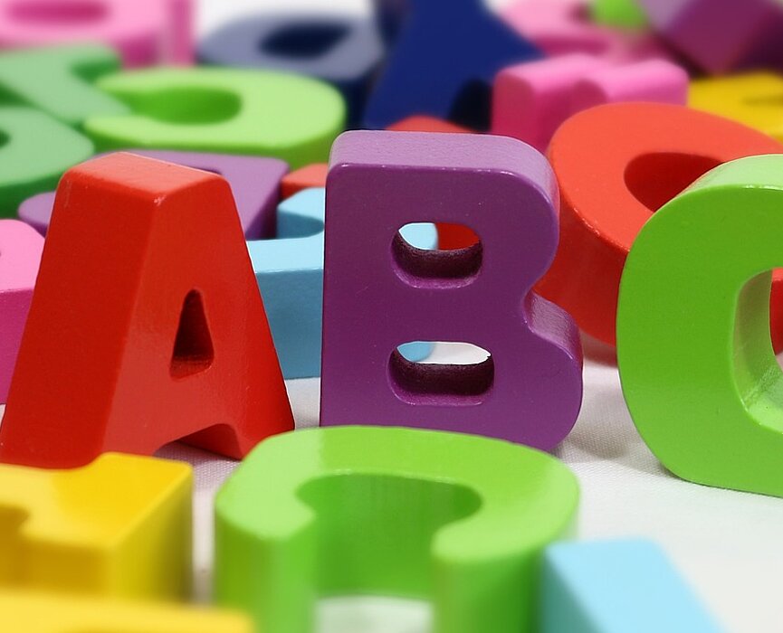 letras coloridas embaralhadas ao fundo, com destaque para as letras A, B e C em primeiro plano