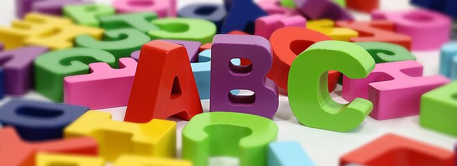 letras coloridas embaralhadas ao fundo, com destaque para as letras A, B e C em primeiro plano