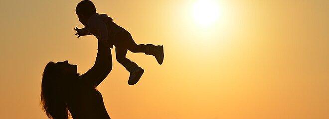 mulher segura seu filho no alto na praia com por do sol ao fundo