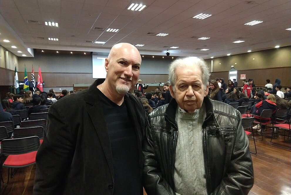 Um senhor de cabelo branco ao lado de um homem em pé
