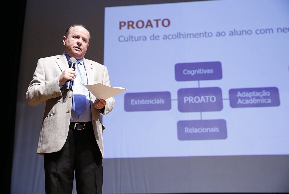 reitor ao palco com telão ao fundo