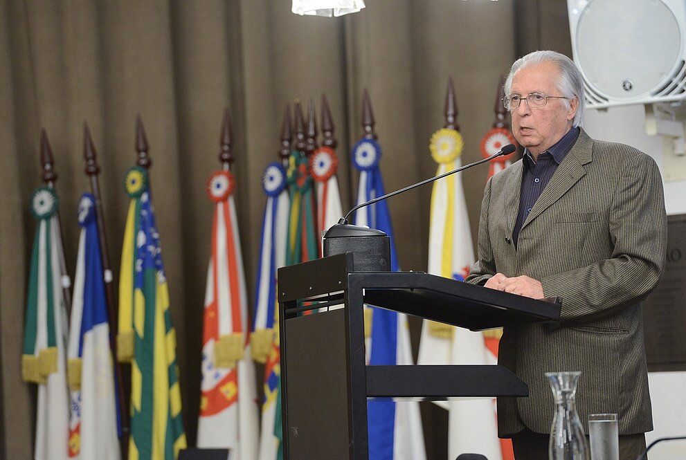 homem discursando ao púlpito com bandeiras ao fundo