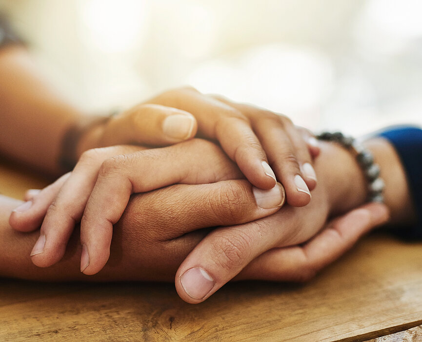 Duas pessoas segurando as mãos, apoiadas em uma mesa.