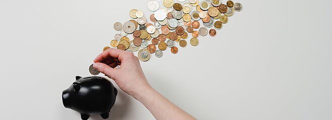 A imagem apresenta um cofre em formato de porco com moedas ao seu redor. 