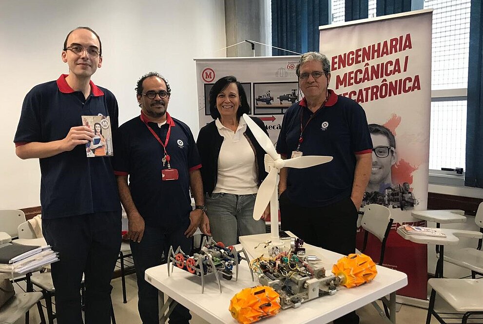 Quatro professores de Engenharia Mecânica reunidos em frente do projeto do curso.