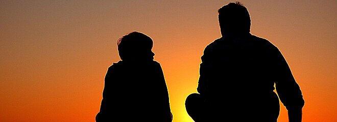 silhueta de pai e filho sentados contra um por do sol