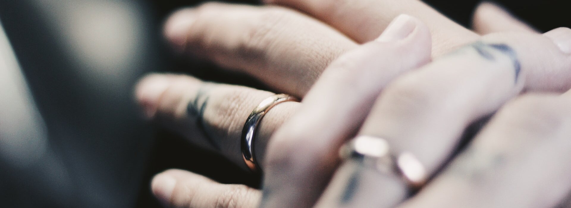 a foto mostra a mão de duas pessoas em close usando alianças de casamento e sobrepostas uma a outra