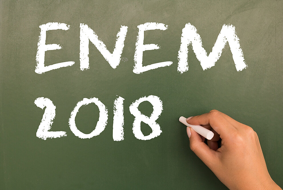 Mão segurando giz com a inscrição "Enem 2018" no quadro negro