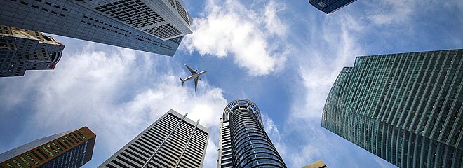 Imagem feita de baixo para cima mostrando vários prédios e um avião passando no céu