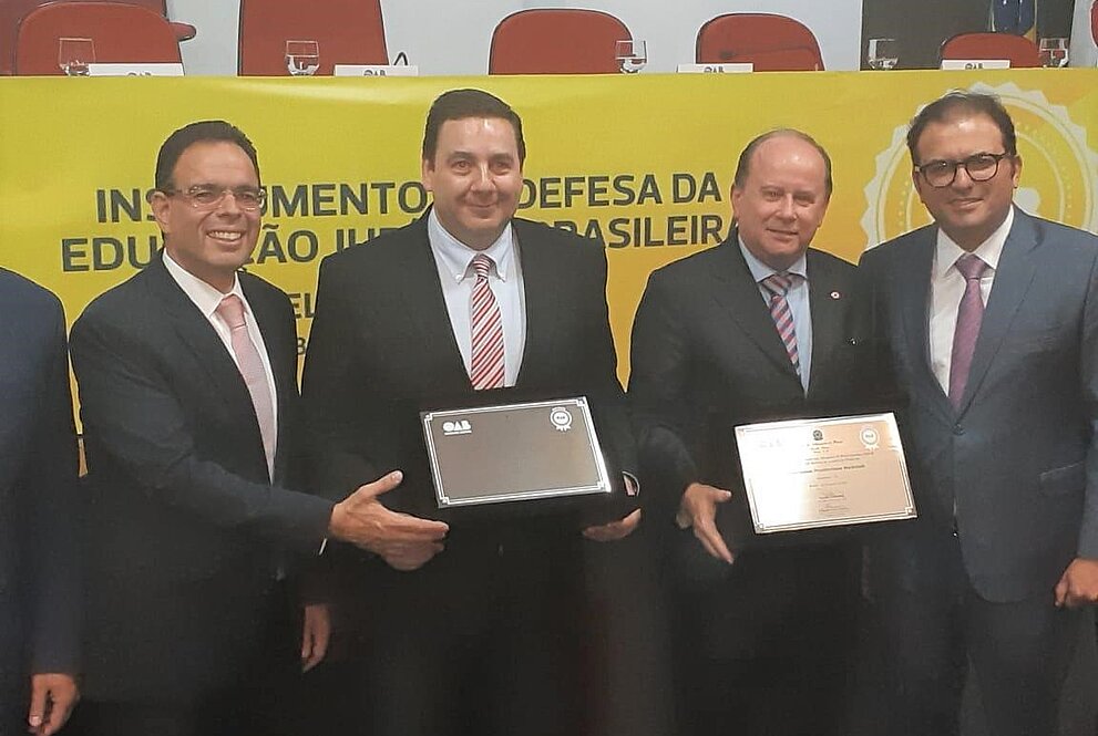 Autoridades da OAB e do Mackenzie posam para foto segurando placas de reconhecimento da universidade