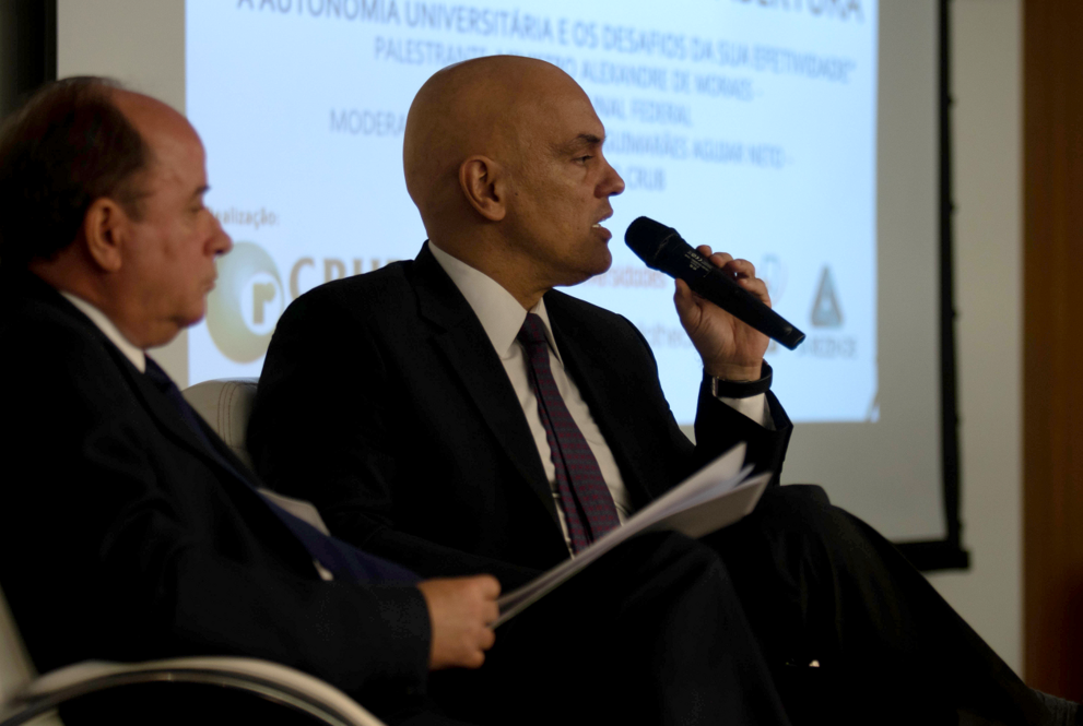 Dois homens sentados olhando para frente estando um segurando o microfonw