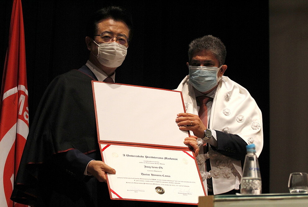 Homem entrega para outro um certificado 
