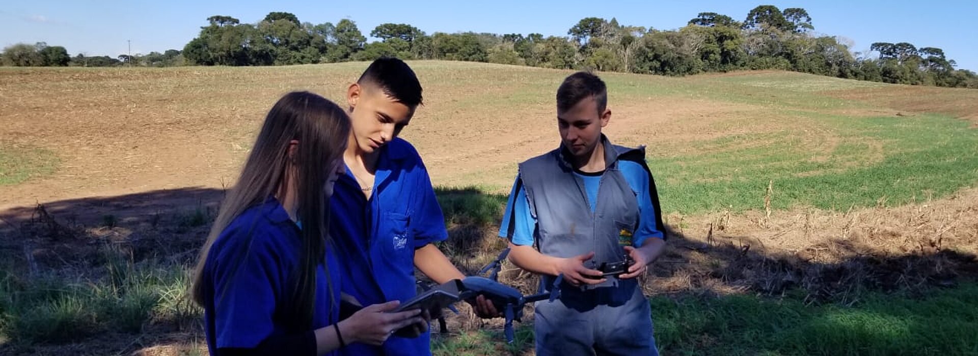 Três pessoas em uma fazenda com um drone na mão