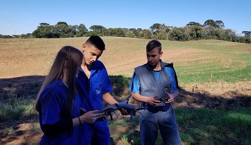 Três pessoas em uma fazenda com um drone na mão