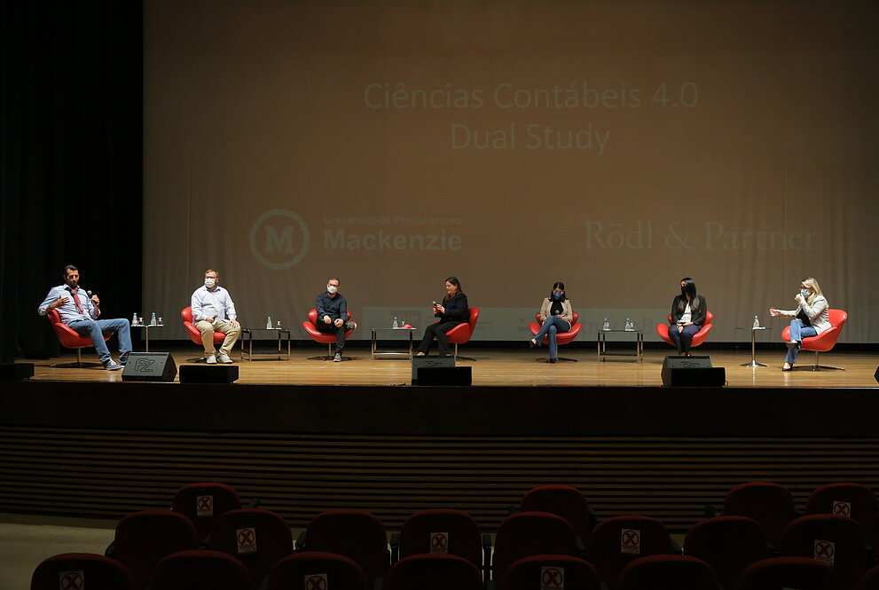Pessoas assentadas em meio círculo conversam sobre um tema