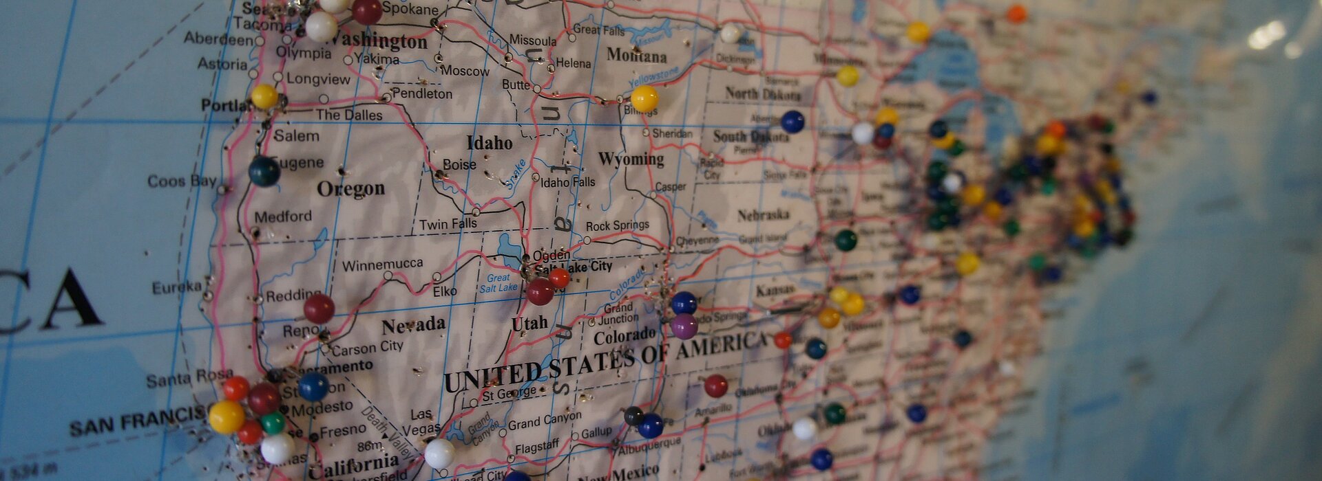 Foto mostra o mapa dos Estados Unidos com vários alfinetes redondos coloridos.  