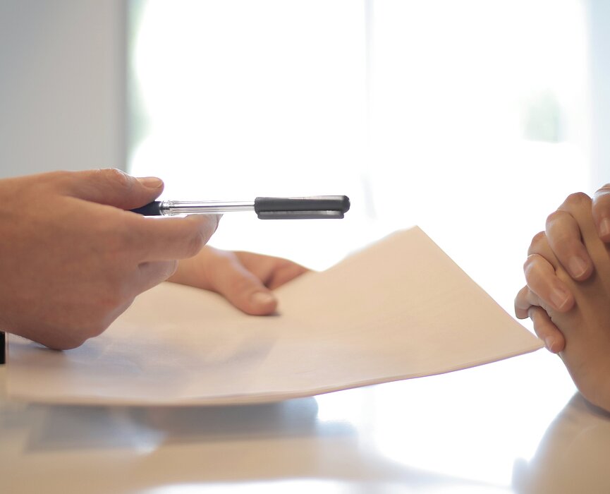 A imagem apresenta uma pessoa prestes a assinar um contrato de emprego.