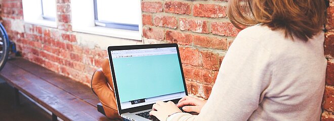 Uma menina mexe no notebook sentada próxima de uma janela