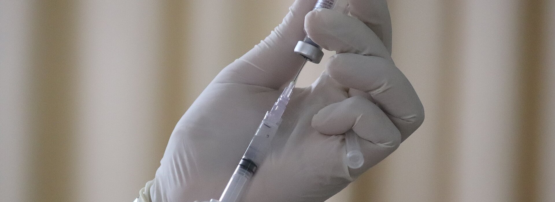 Mão de profissional da saúde segurando uma dose da vacina 