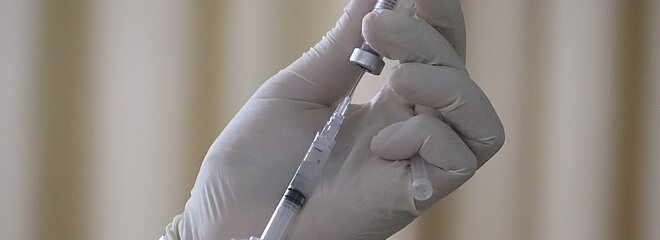 Mão de profissional da saúde segurando uma dose da vacina 