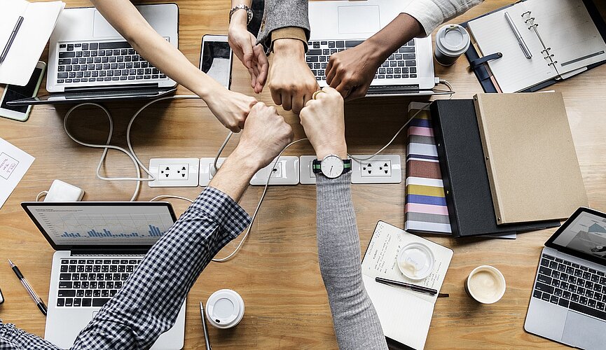 várias pessoas unem suas mãos no meio de uma mesa, com vários notebook e cadernos de negócios na mesa 