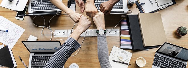 várias pessoas unem suas mãos no meio de uma mesa, com vários notebook e cadernos de negócios na mesa 