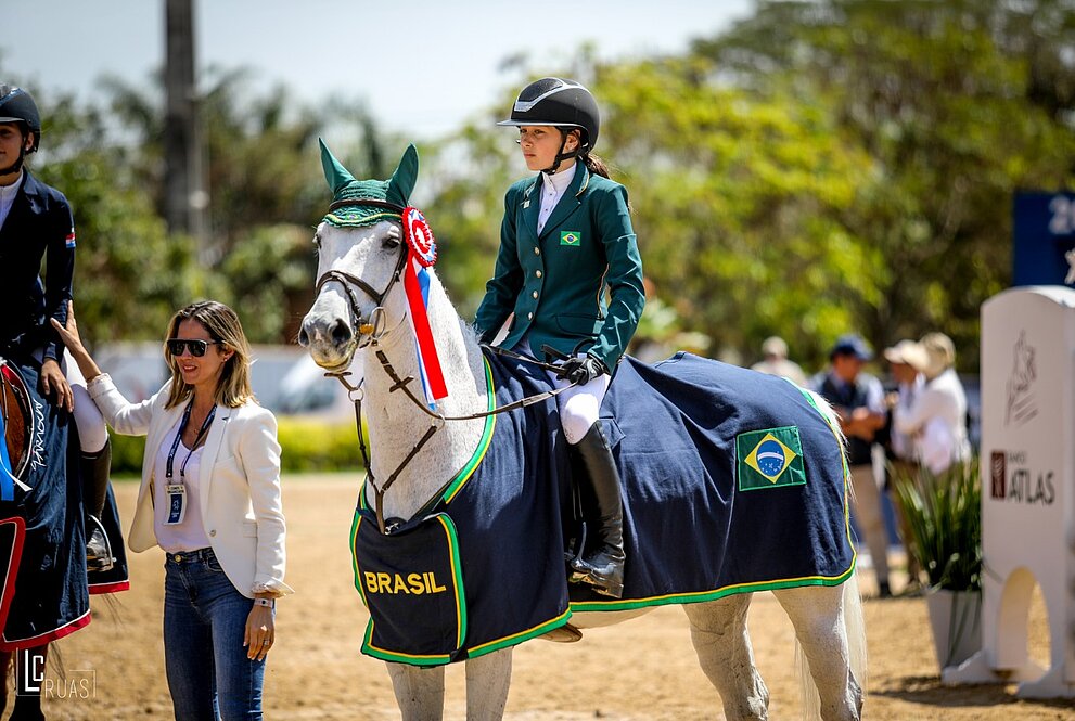 Uma menina montada em um cavalo em competição de saltos com barreiras