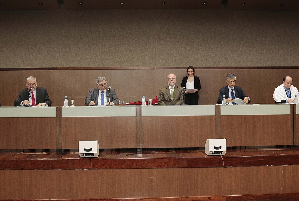 Diversos homens assentados em uma mesa cumprida com forro branco