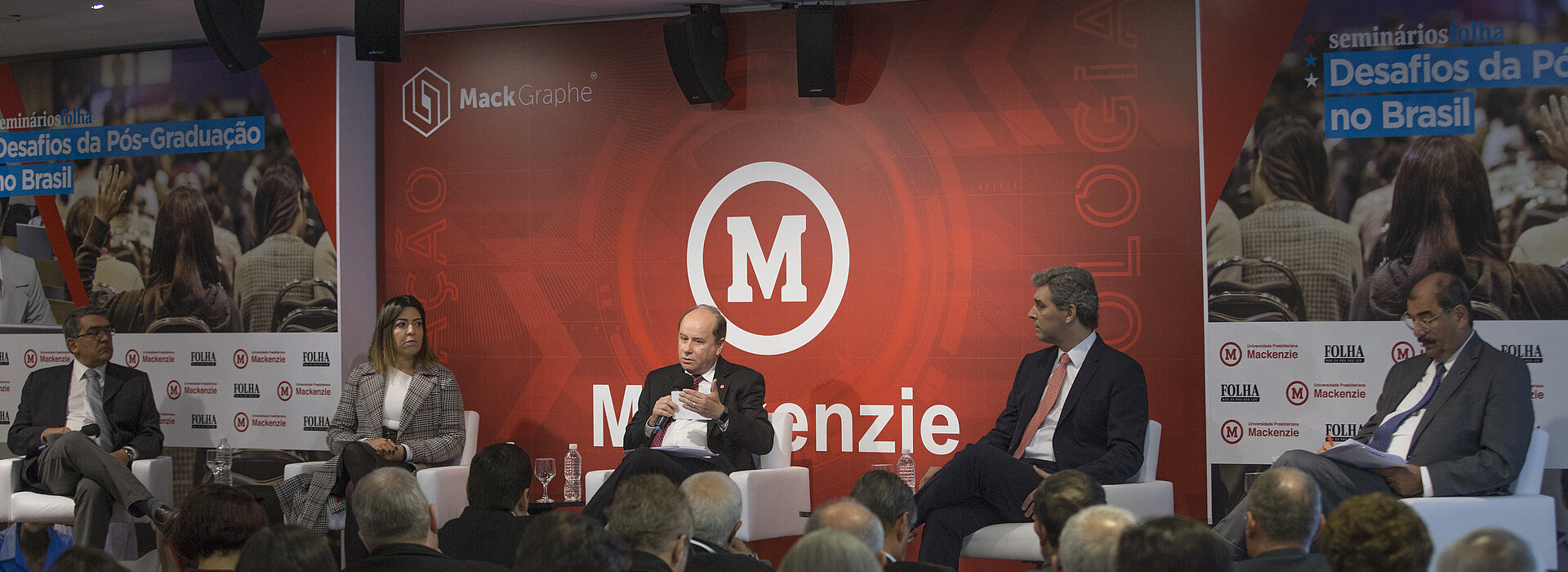 autoridades debatendo no palco com plateia cheia