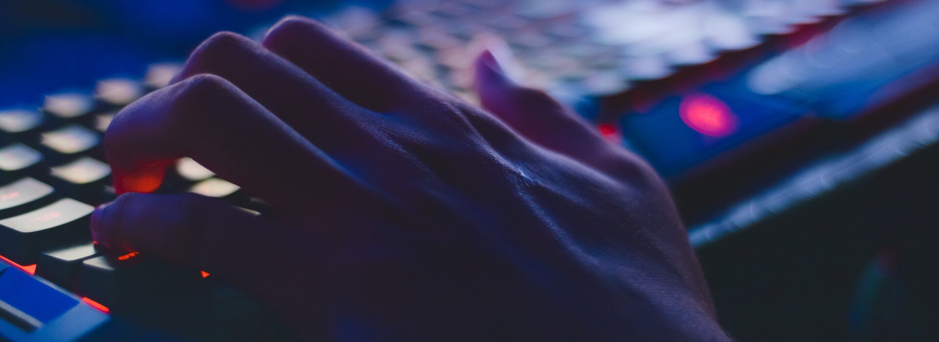 A foto mostra uma mão digitando em um teclado. A luz da foto está bem baixa. 