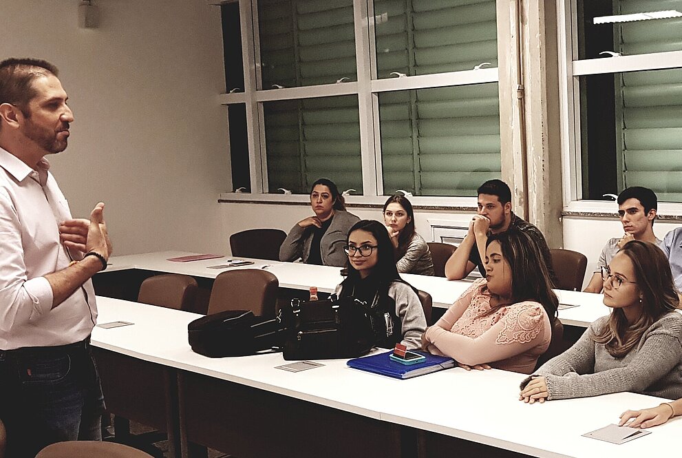 Palestra Thiago Salgado de pé conversando com participantes sentados.