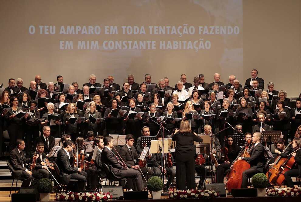 Visão de frente da orquestra e coral, telão ao fundo