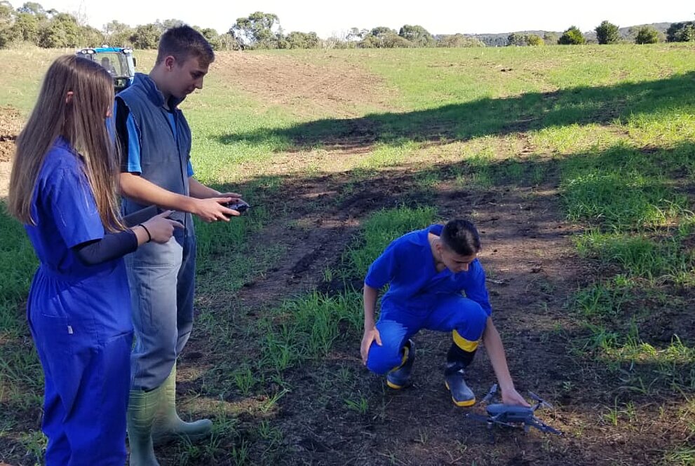Três pessoas em uma fazenda com um drone na mão