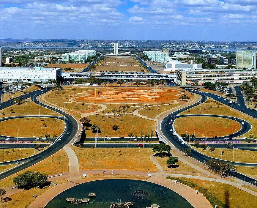 imagem do alto do planalto, em Brasília. o céu está azul, com algumas poucas nuvens brancas e pode-se ver os prédios, ruas e praças