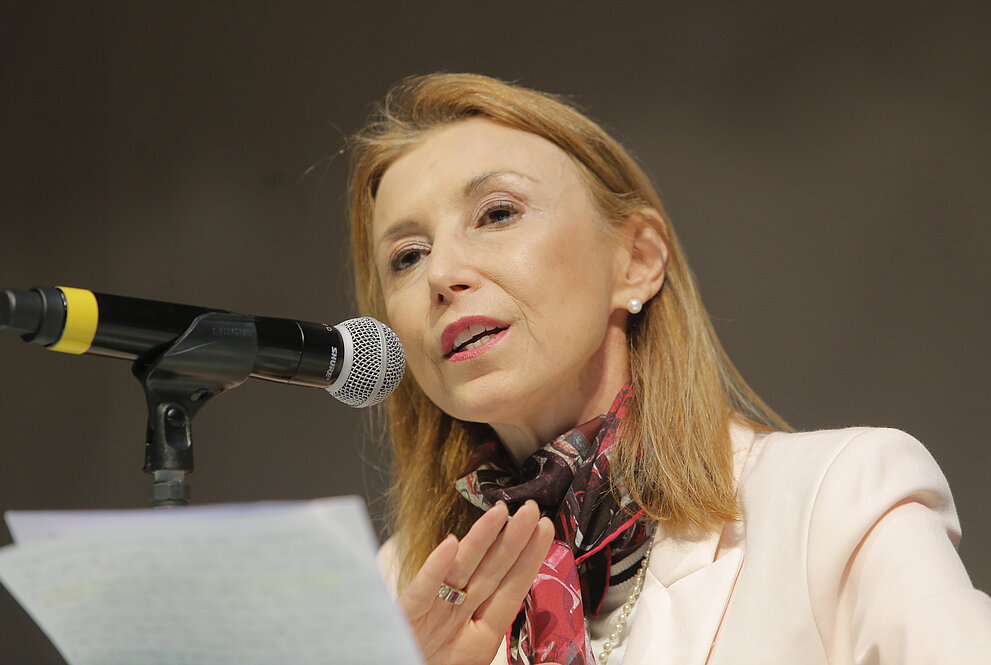 mulher discursa sentada à mesa de autoridades