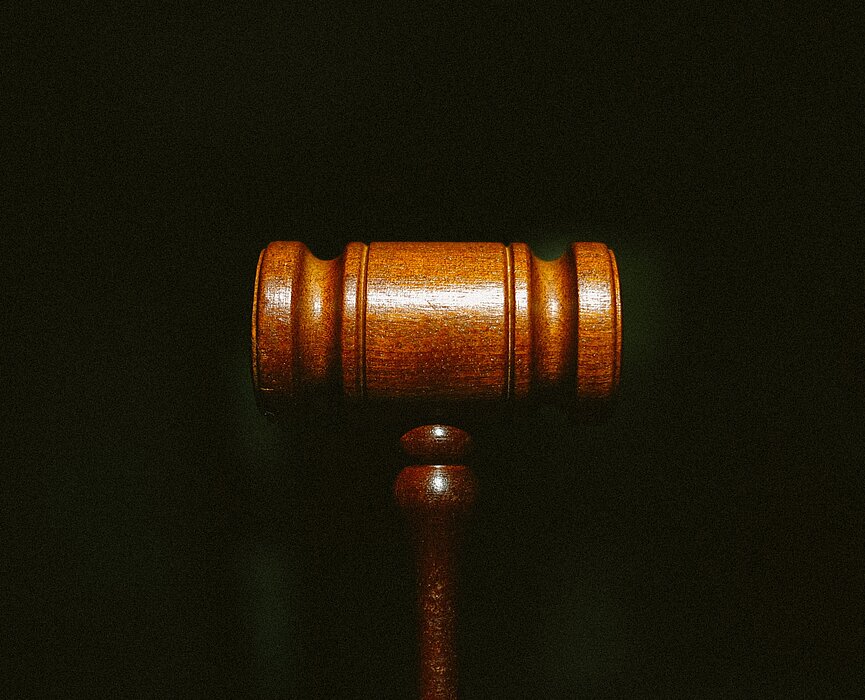 Na foto um malhete marrom, o famoso martelo utilizado pelo juiz, está centralizado no meio. O fundo é todo escuro e o foco está somente no martelo.