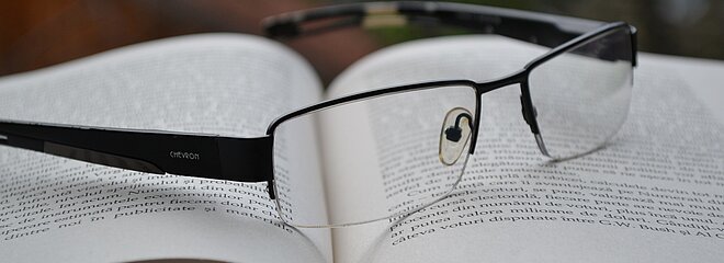 Imagem com um livro aberto e um óculos de grau em cima