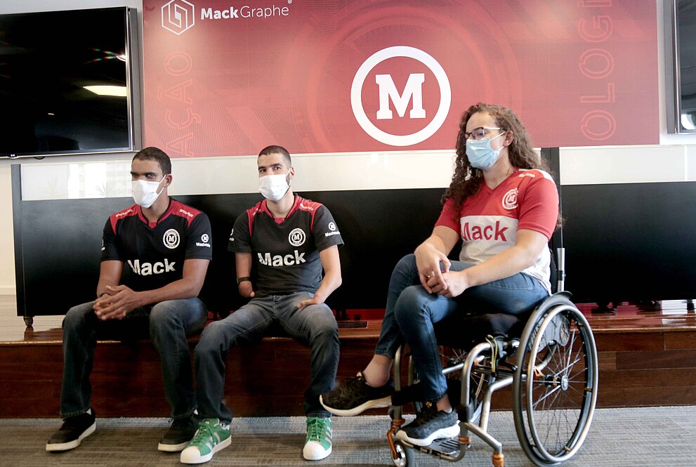 três pessoas assentadas com símbolo do Mackenzie ao fundo