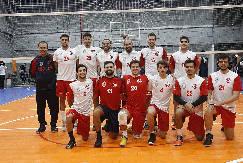 Mackenzistas competidores posando para foto, em frente à rede de voleibol.