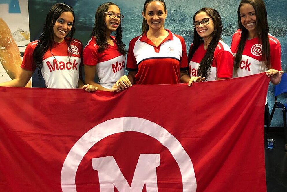 Atletas com treinadora segurando a bandeira do Mackenzie.
