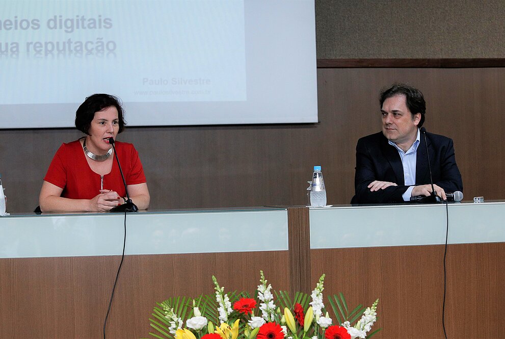 Professores sentados à mesa durante apresentação