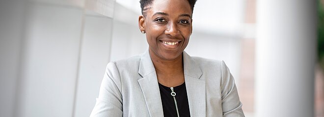 Uma mulher está em um ambiente claro, sorrindo e olhando para a câmera. 